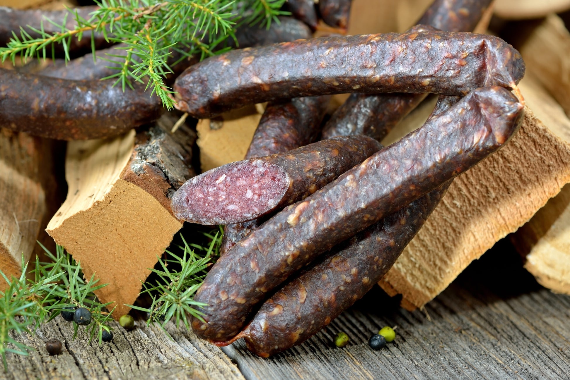Originale dunkel geräucherte Südtiroler Kaminwurzen vor Holzscheite mit frischem Wacholder platziert